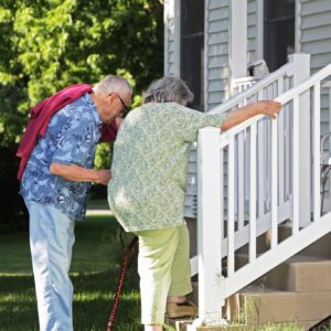 Elderly senior couple arriving home. He is helping her climb slowly up their back porch steps.