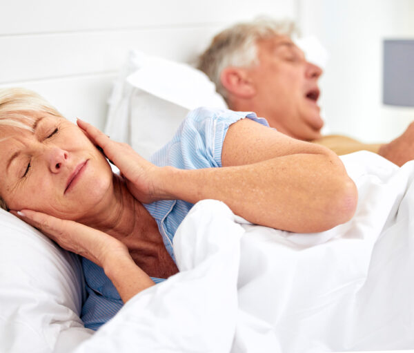 Snoring, problem and woman with frustrated with noise, sound or husband sleeping in bed with wife. Elderly, couple and man snore in sleep in retirement home bedroom and lady with hands on ears